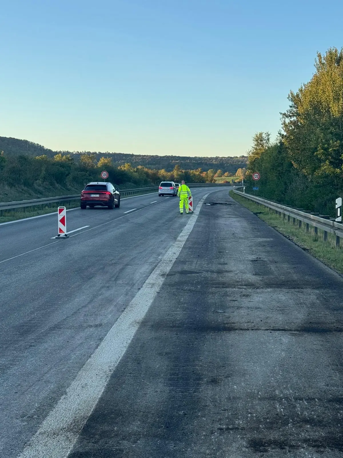 Person in gelber Warnkleidung hält am Fahrbahnrand einer Autobahn eine Leitbake, während auf den Fahrstreifen daneben Autos vorbeifahren; weiter links steht eine Leitbake auf der Fahrstreifenmarkierung